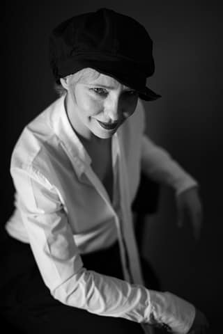 Portret aktorki w trakcie modowej sesji zdjęciowej Czarno-biały kobiecy portret przedstawiający aktorkę w czarnym kaszkiecie i białej koszuli, pozującą do ujęcia w trakcie sesji zdjęciowej w Warszawie.