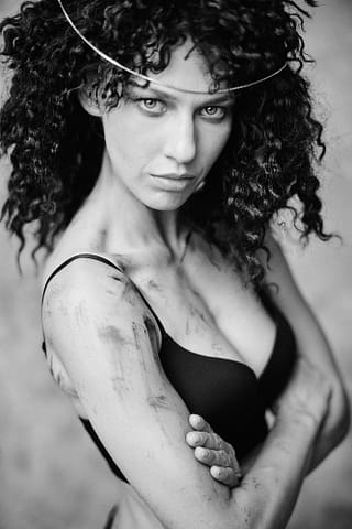 Stylizowana sesja kobieca aktorki. Warszawa. Czarno-biały portret pewnej siebie kobiety: kobieta z kręconymi włosami pozuje w bieliźnie. Fotografia kreacyjna, na której aktorka występuje w stylizacji filmowej przywodzącej na myśl filmy z serii Mad Max. Sesja aktorska w studio w Warszawie.