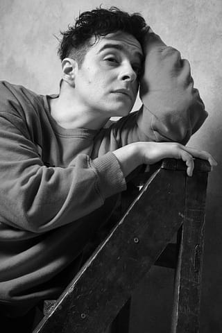 Czarno-biały portret aktorski w studio w Warszawie Mężczyzna opierający się o drabinę, uchwycony na zdjęciu aktorskim w czerni i bieli, emanuje ponadczasową elegancją i kinowym stylem.