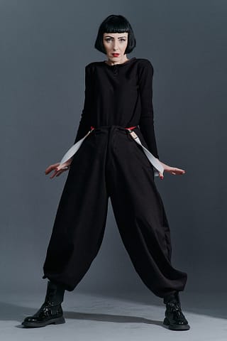 Studyjne sesje zdjęciowe stylizacji modowych Kobieta z krótką czarną fryzurą pozuje pewnie w luźnych czarnych spodniach, czarnej bluzce z długim rękawem i czarnych butach, ucieleśniając siłę fotografii w służbie mody.